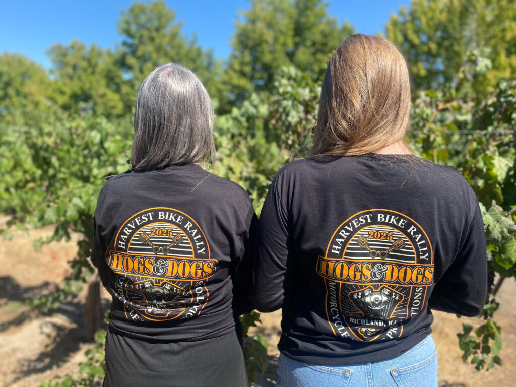 Two women wearing Harvest Bike Rally shirts in vineyard