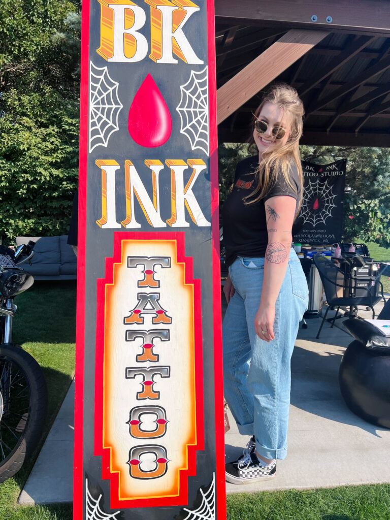 Woman standing beside BK Ink Tattoo sign
