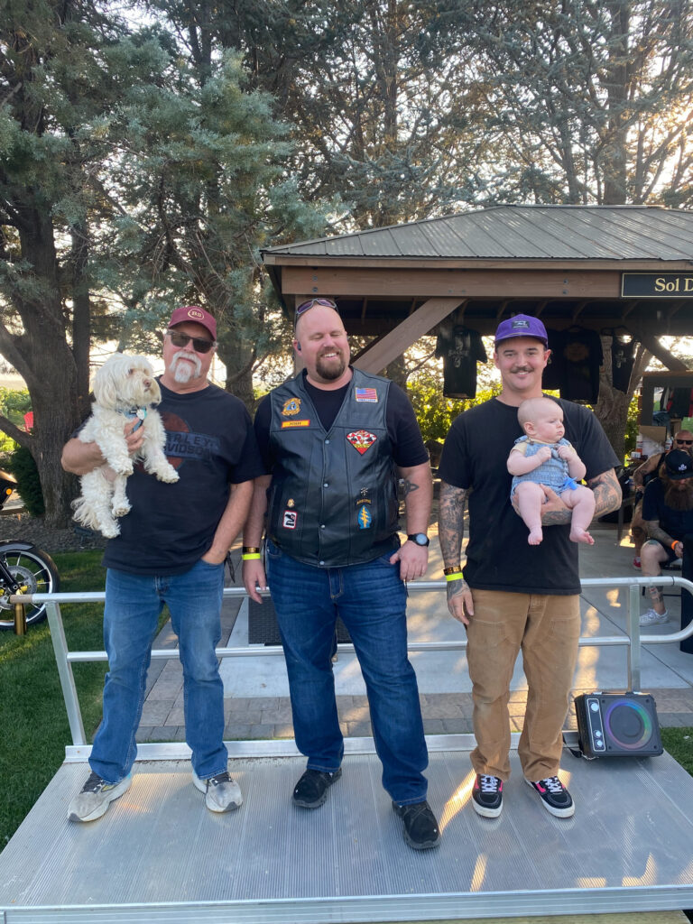 Three men holding dog and baby outdoors