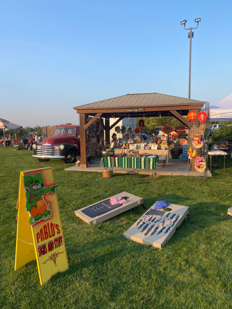 Outdoor market booth with vintage truck and cornhole boards