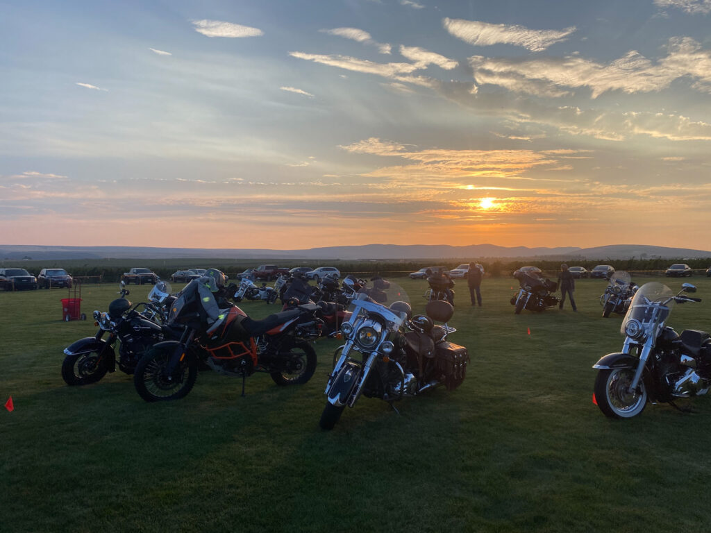 Motorcycles parked on grassy field at sunset