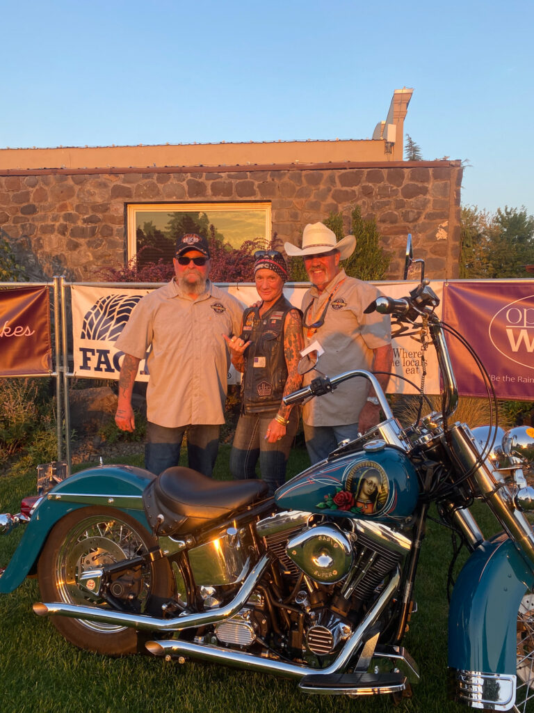 Three bikers posing beside vintage motorcycle at sunset