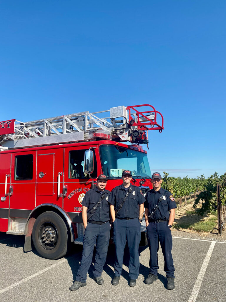 Three firefighters beside red ladder fire truck