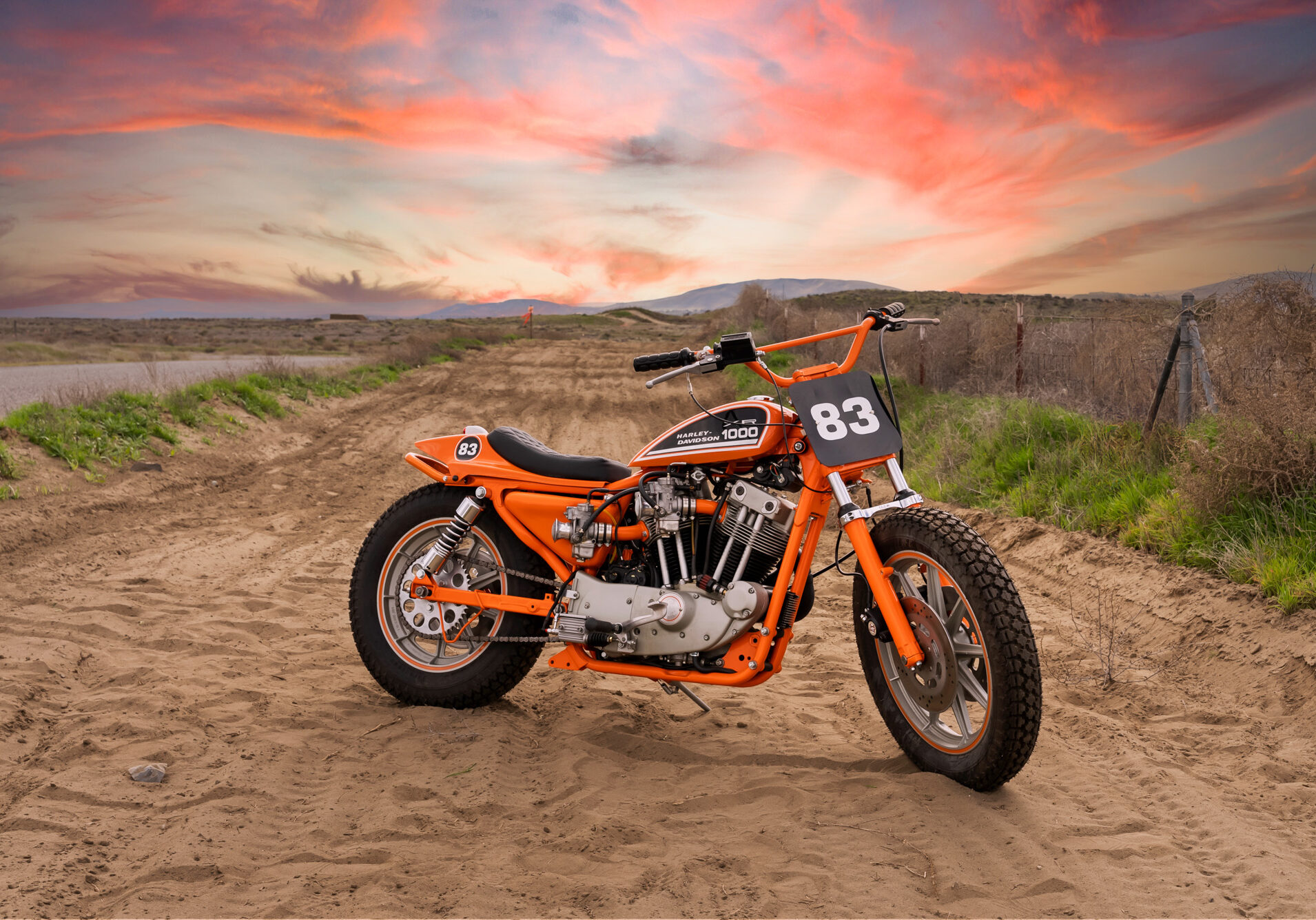 Orange motorcycle on sandy landscape at sunset